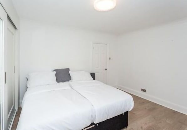 A bedroom with a single bed, white walls, a door, and a light fixture.