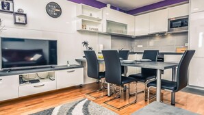 A modern kitchen with white cabinets, a dining table with chairs, a flat-screen TV, and a clock on the wall. - Apartment Mare by Interhome (Zadar)