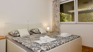 A neatly made bed with patterned bedding, a bedside lamp, and a window with curtains. - Apartment Mare by Interhome (Zadar)