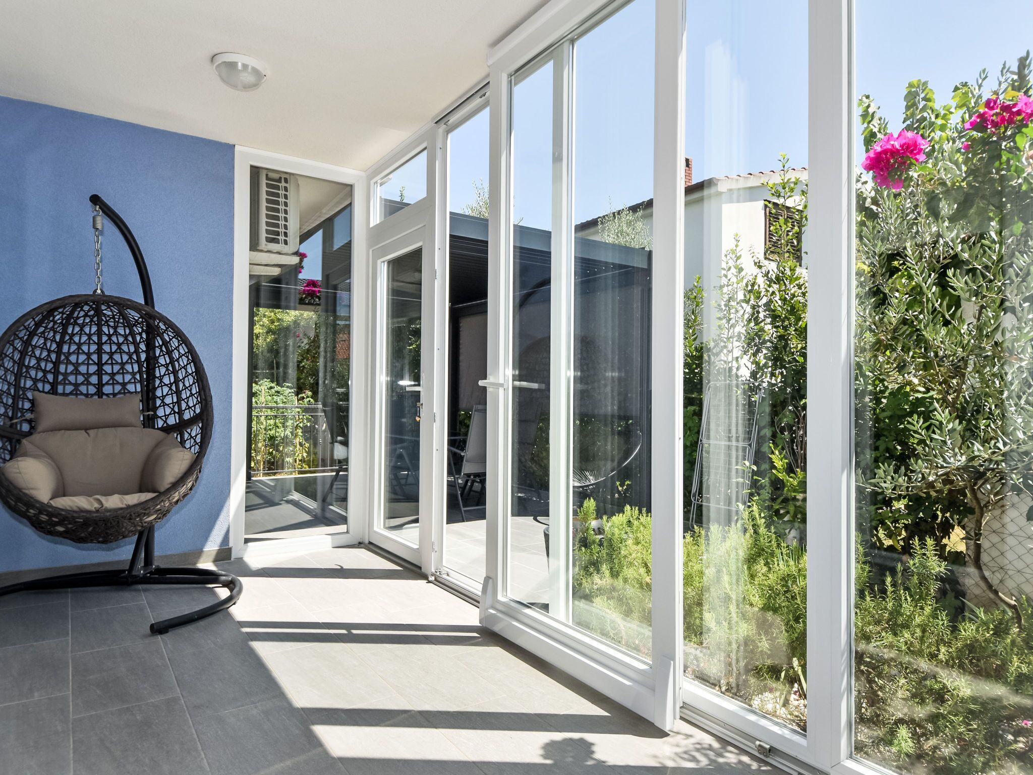 Un intérieur moderne avec un fauteuil suspendu, de grandes portes vitrées donnant sur un jardin et un mur bleu.