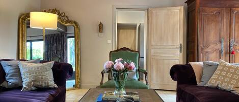 A living room with two dark purple sofas, a green armchair, and a coffee table with books and a vase of flowers.