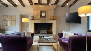 A living room with two purple sofas, a coffee table, a fireplace, and a television mounted on the wall. - Stylish farmhouse with pool, sleeps 8-10 (Verneuil-sur-Indre)