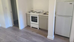 Una cocina pequeña con estufa, horno y refrigerador blancos, suelo de madera clara y una puerta que da a otra habitación.