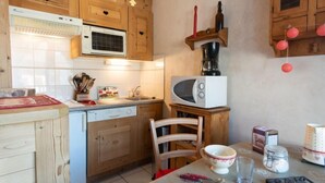A kitchen with wooden cabinets, a microwave, a stove, and a table with a chair. - Bel Alp 23 by Interhome (Saint Gervais)