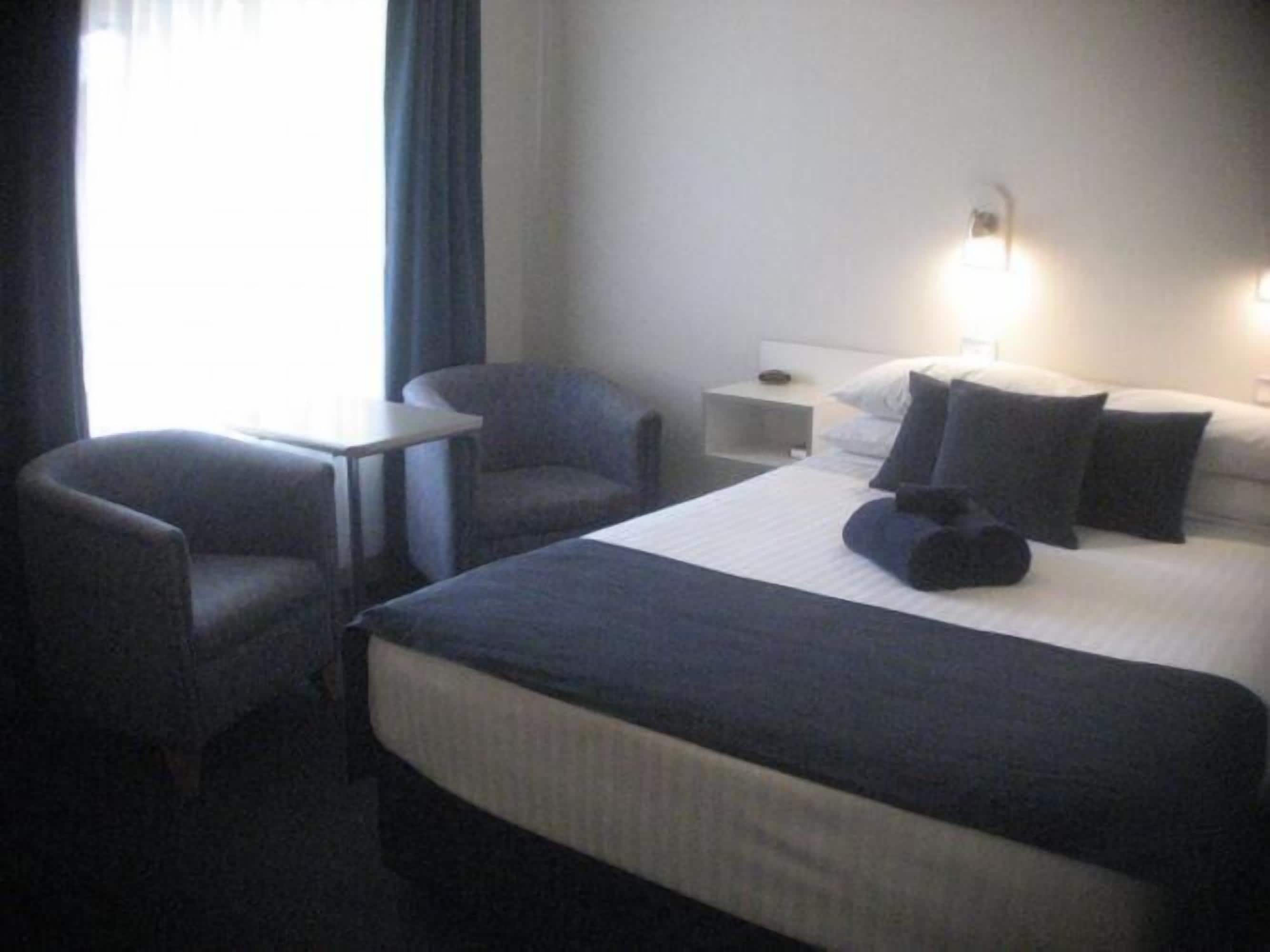 Een hotelkamer met een bed, twee fauteuils, een tafeltje en een nachtkastje.