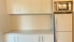 Een keuken met witte kasten, een magnetron en een koelkast.