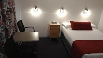 Une chambre d’hôtel comprenant un lit, un bureau, une chaise, une table de chevet et un luminaire fixé au mur.