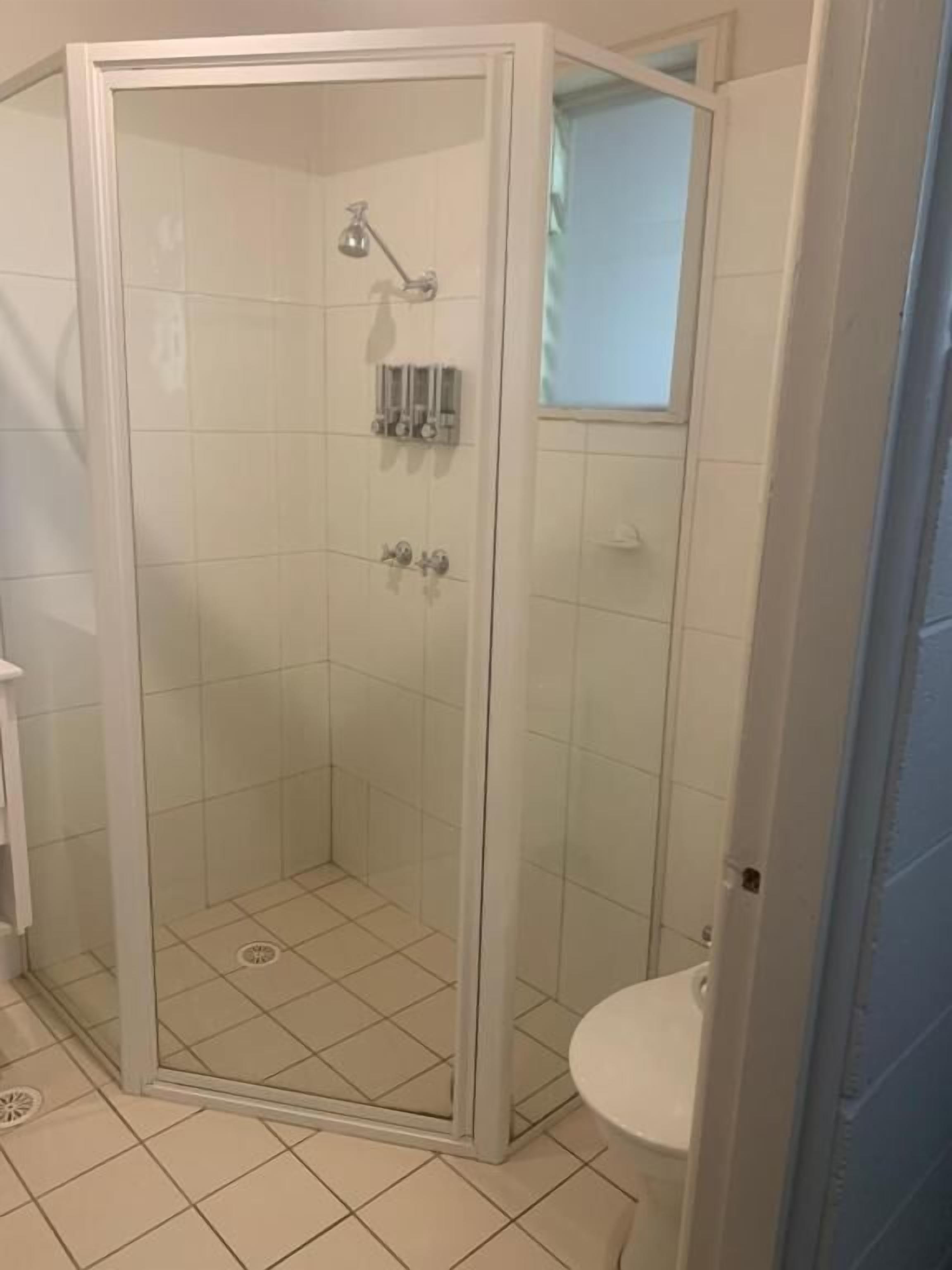 A glass-enclosed shower stall with a white toilet and a small window above the sink.