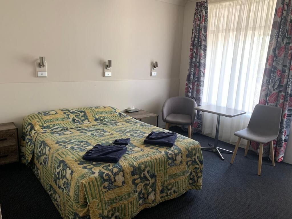 A hotel room with a bed, a desk, a chair, and a window with curtains.