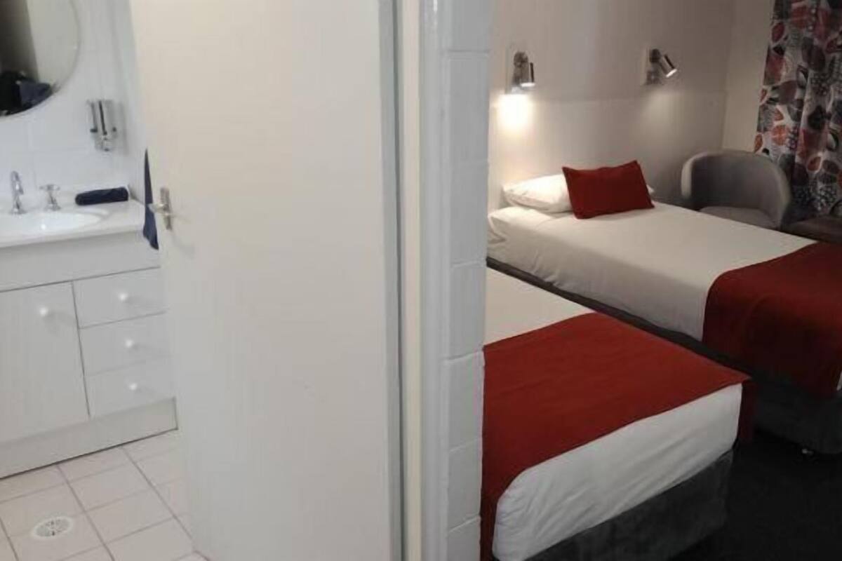 Une chambre d’hôtel avec deux lits, une salle de bain équipée d’un lavabo et d’un miroir, et une chaise.