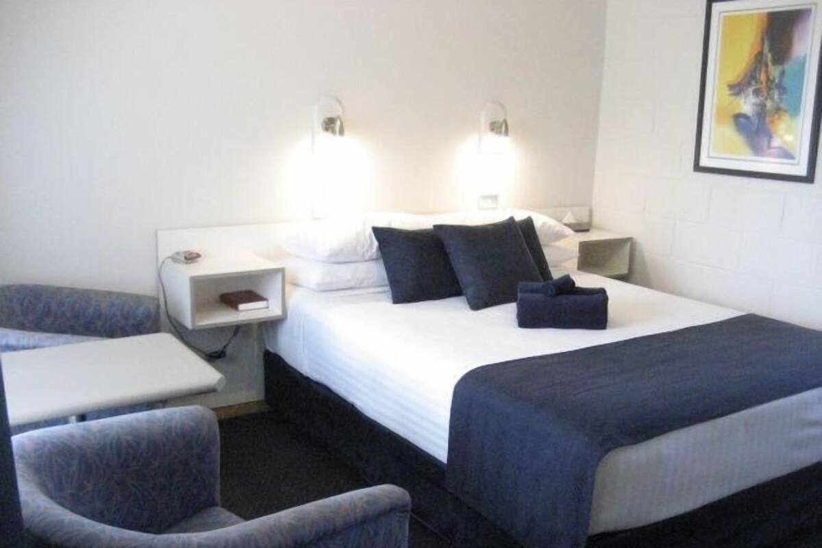 Une chambre d’hôtel comprenant un lit, deux tables de chevet, une chaise et une œuvre d’art accrochée au mur.