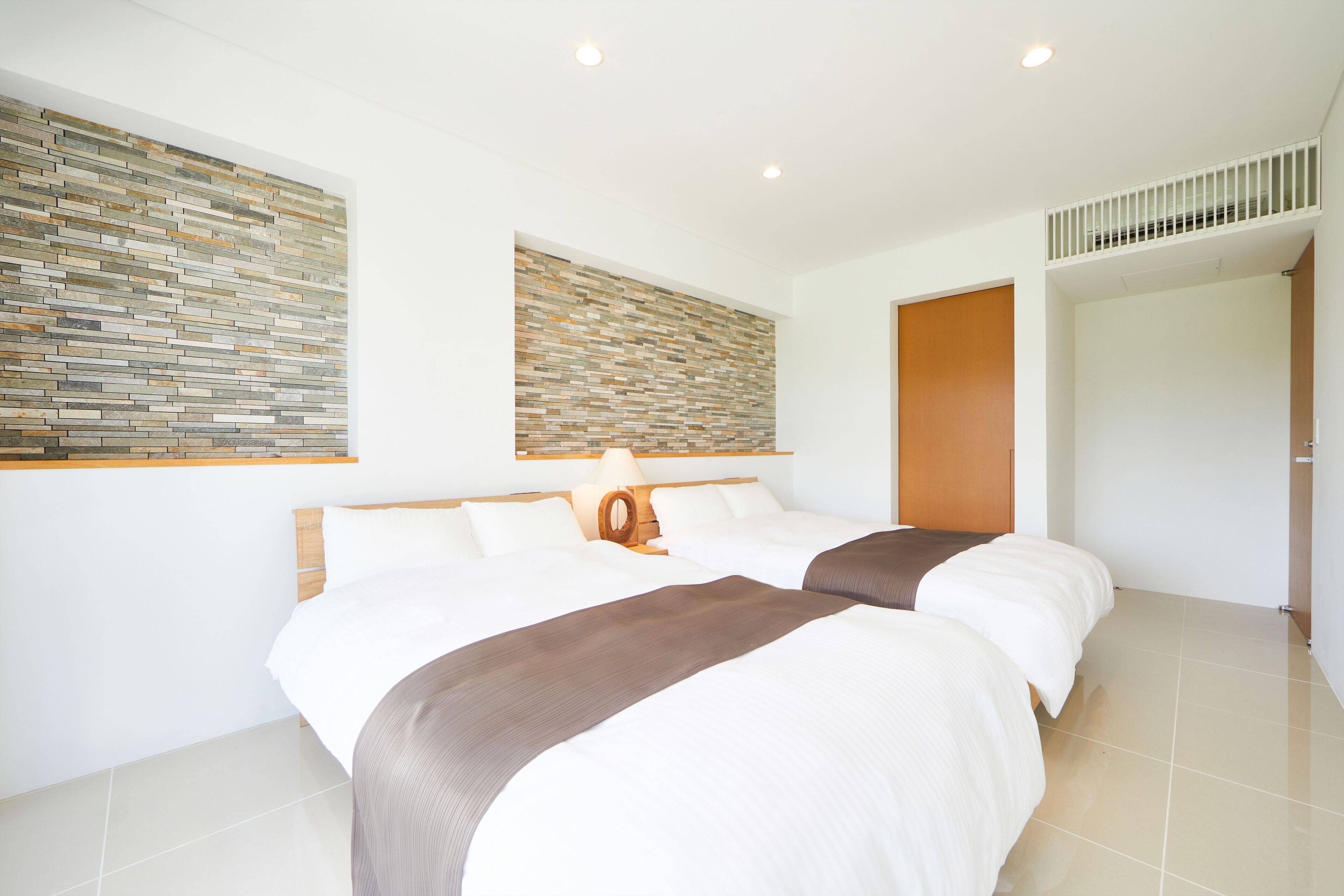 A modern hotel room with a large bed, a wooden headboard, a stone wall, and a wooden door.