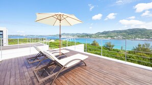 A wooden deck with lounge chairs and an umbrella, overlooking a coastal landscape with a bridge and hills. - E-horizon Resort Premium sesokoD (Motobu)