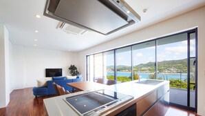 A modern kitchen with a large island, a dining area with a view, and a living space with a sofa and TV. - E-horizon Resort Premium sesokoD (Motobu)
