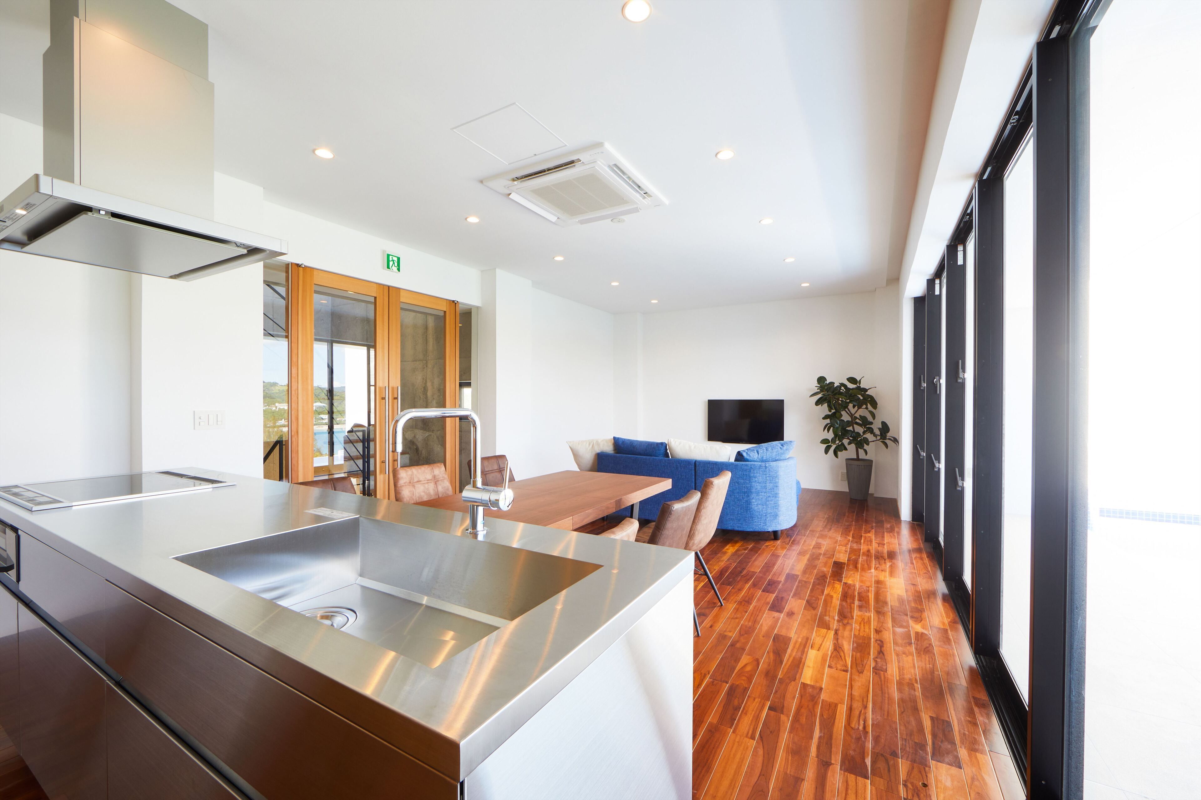 A modern kitchen with a stainless steel island, wooden flooring, and a dining area with a blue sofa and chairs.