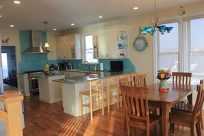 A spacious kitchen with wooden chairs, a dining table, and a large window.