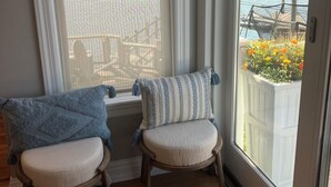 Ein Zimmer mit Blick auf ein Gewässer, zwei Stühle mit Kissen und ein Fenster mit Blick auf einen Steg und Blumen.