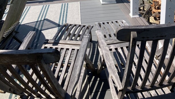 Eine Terrasse mit Holzstühlen und einem Topfpflanzen, mit Blick auf ruhiges Gewässer und darin liegende Boote.