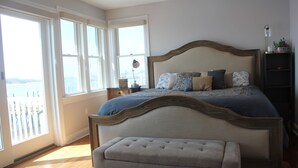 Ein Schlafzimmer mit einem großen Bett, einem Nachttisch, einer Bank und Blick ins Freie.