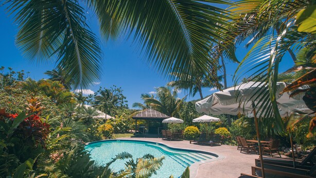 A swimming pool surrounded by lush greenery and outdoor seating areas. - Villa TORU beautiful tropical style villa with outdoor bath, on the sunset side (Rarotonga)