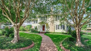 A two-story house with a front porch, surrounded by a brick pathway and trees. - Sleeps 19 Guests ~ Prime Location Near Lake & FSC (Lakeland)