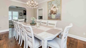 A dining room with a large table, white chairs, a chandelier, and a floral painting on the wall. - Sleeps 19 Guests ~ Prime Location Near Lake & FSC (Lakeland)
