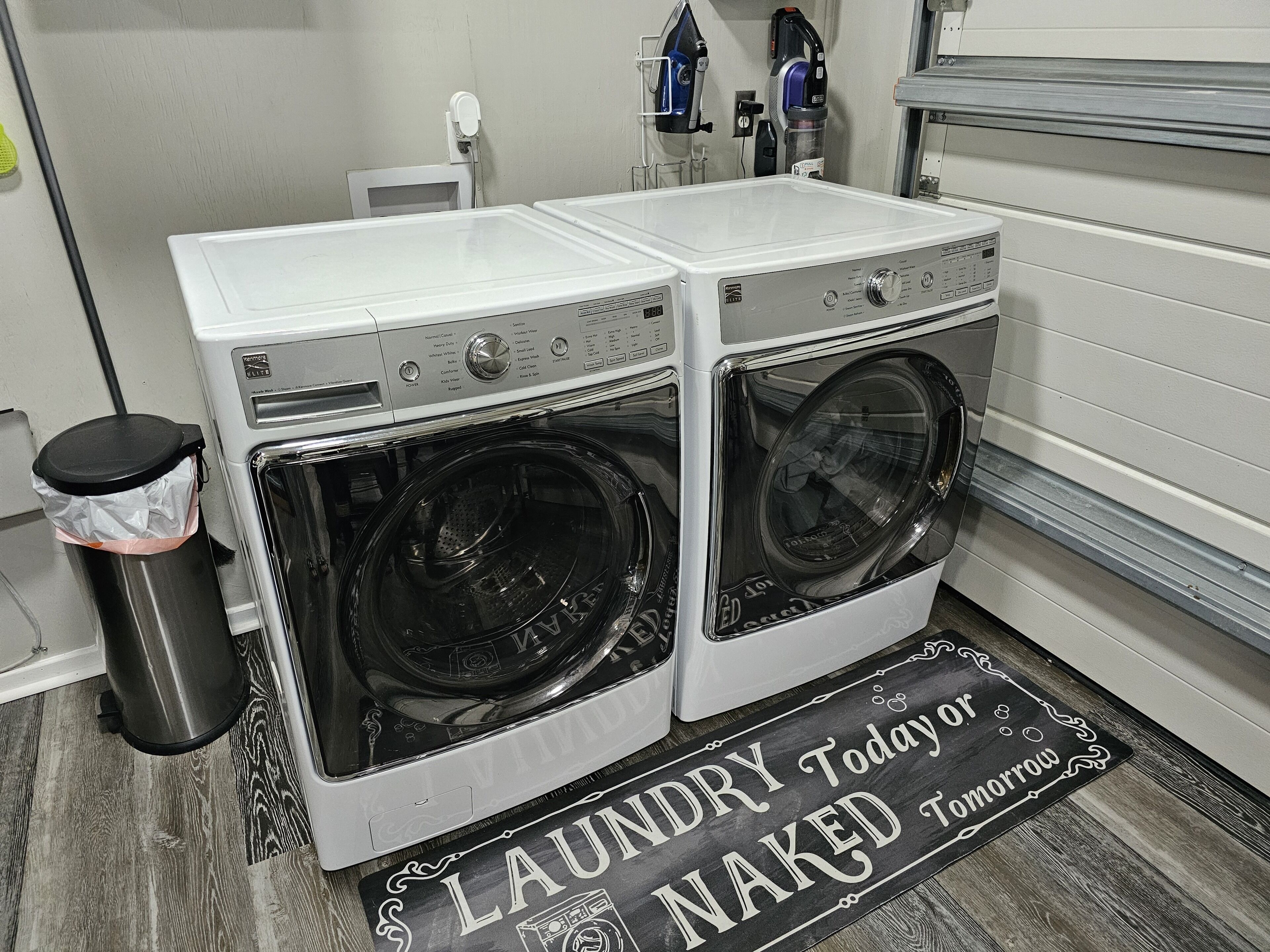A laundry room with two front-loading washing machines and a trash can.