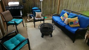 Un patio al aire libre con una parrilla, dos sillas, una mesita y un sofá.