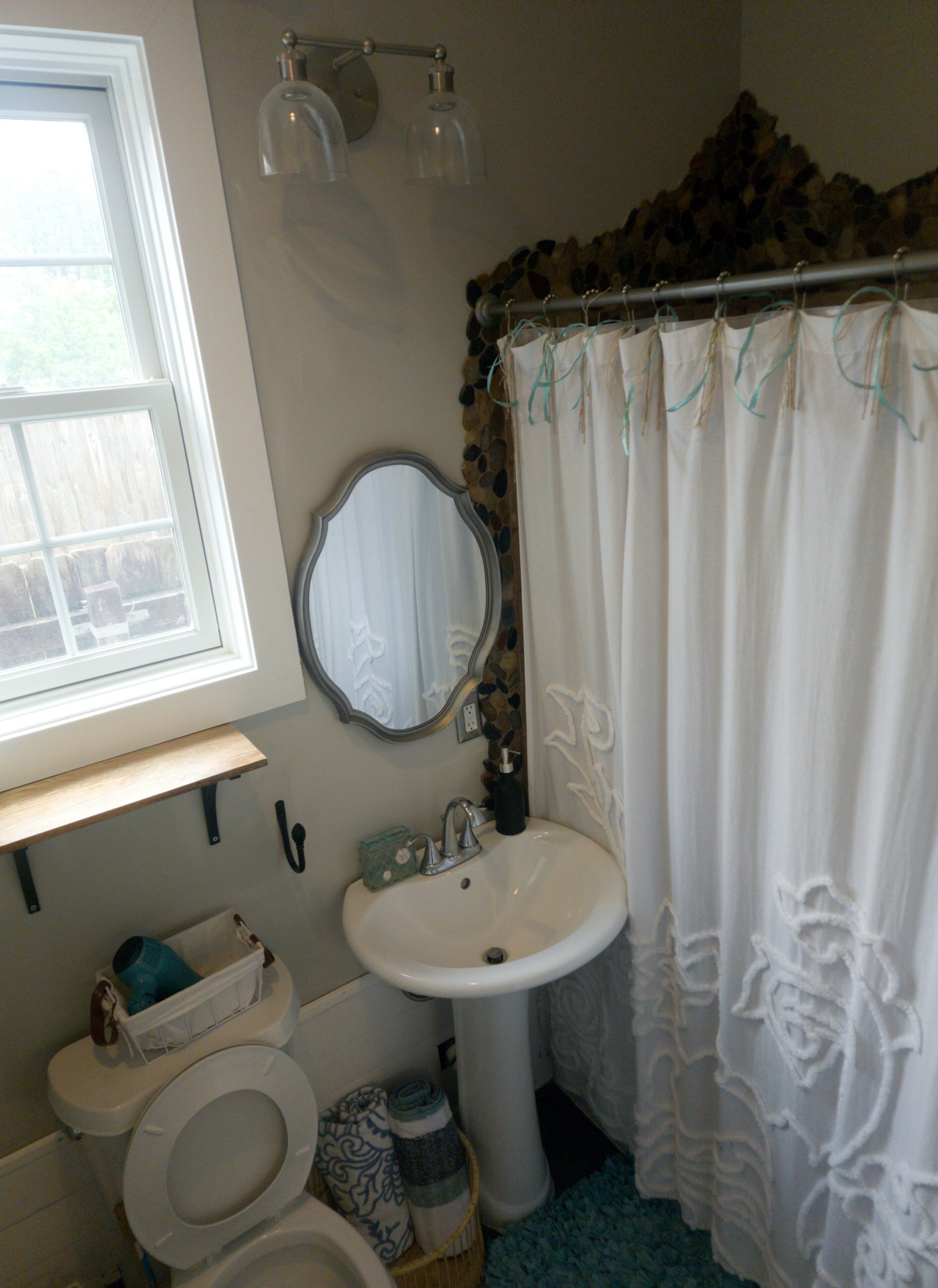 Une salle de bain avec un lavabo blanc, un miroir, des toilettes et un rideau de douche.