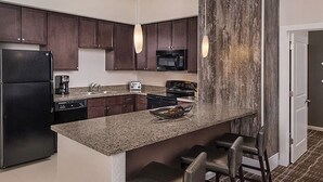 A modern kitchen with dark wood cabinets, a granite countertop, a black refrigerator, a microwave, a stove, and a coffee maker. There are two bar stools and a small island with a bowl of fruit. - Lodge-style First-Class Resort. Gondola outside-SOOOO Convenient! Sleeps 4 (Park City)