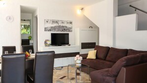 A modern living room with a brown sofa, a dining table with chairs, a TV, and a kitchen area with cabinets and a countertop. - Vacation home Karin by Interhome (Lovran)