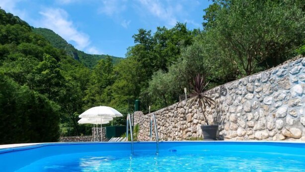 A swimming pool with a stone wall and trees in the background. - Vacation home Karin by Interhome (Lovran)