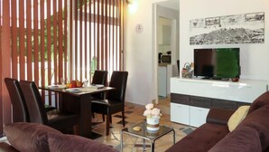 A modern living room with a brown sofa, a dining area with a table and chairs, a TV on a white cabinet, and a decorative vase with flowers. - Vacation home Karin by Interhome (Lovran)
