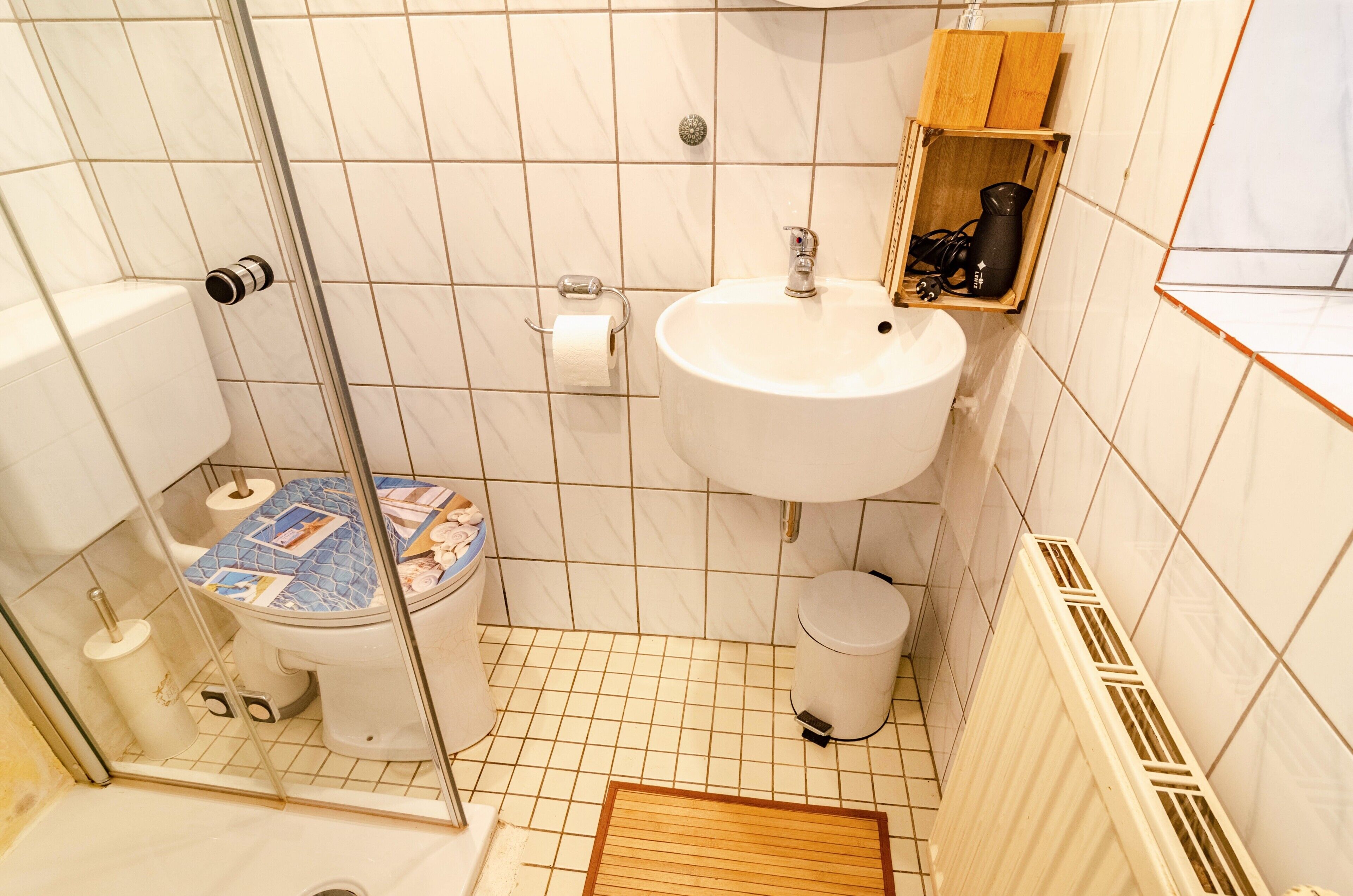 Een badkamer met toilet, wastafel, douche en een klein houten plankje met toiletartikelen.
