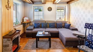 A cozy living room with a sectional sofa, a fireplace, a coffee table, and a clock on the wall. - Vacation Home 'Segelboot' with Garden, BBQ & Wi-Fi (Krummhörn)