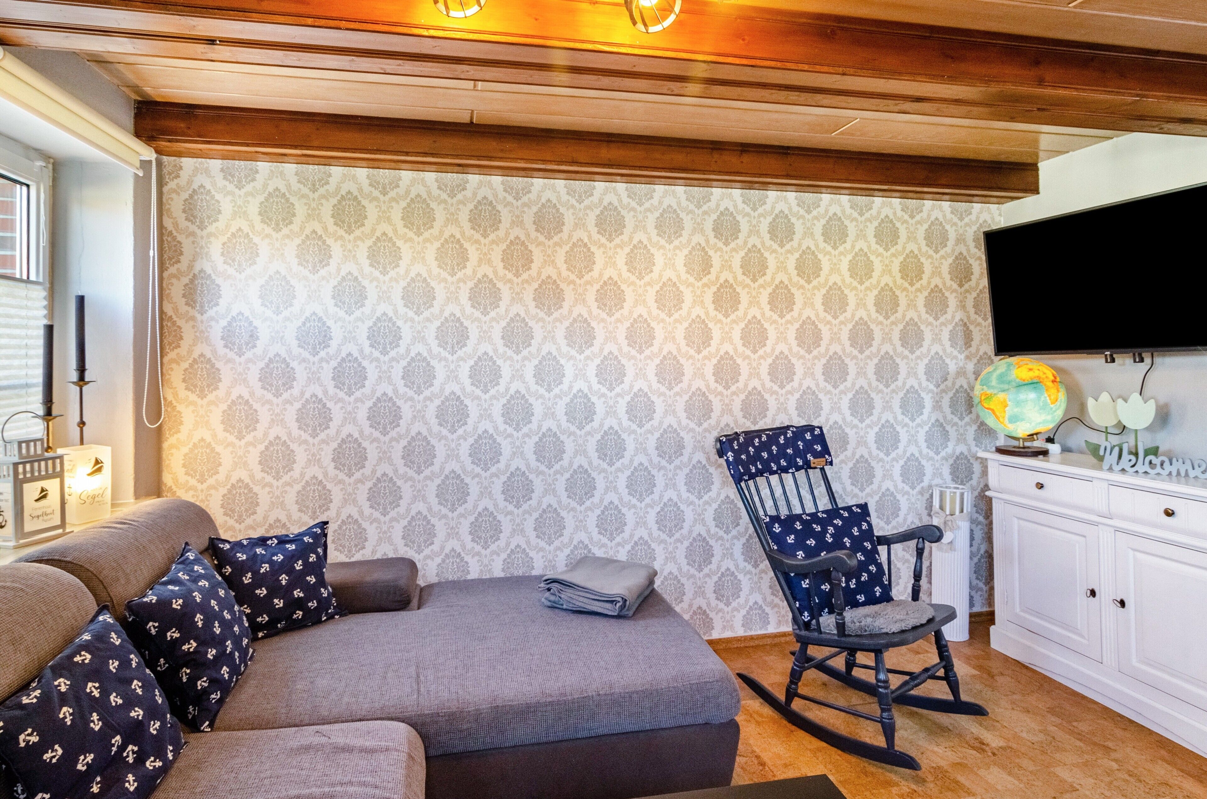 Uma sala de estar acolhedora com um sofá, poltrona de balanço e uma TV de tela plana na parede.