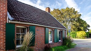 A brick building with green shutters, a tiled roof, and a paved pathway leading to it. - Vacation Home 'Segelboot' with Garden, BBQ & Wi-Fi (Krummhörn)