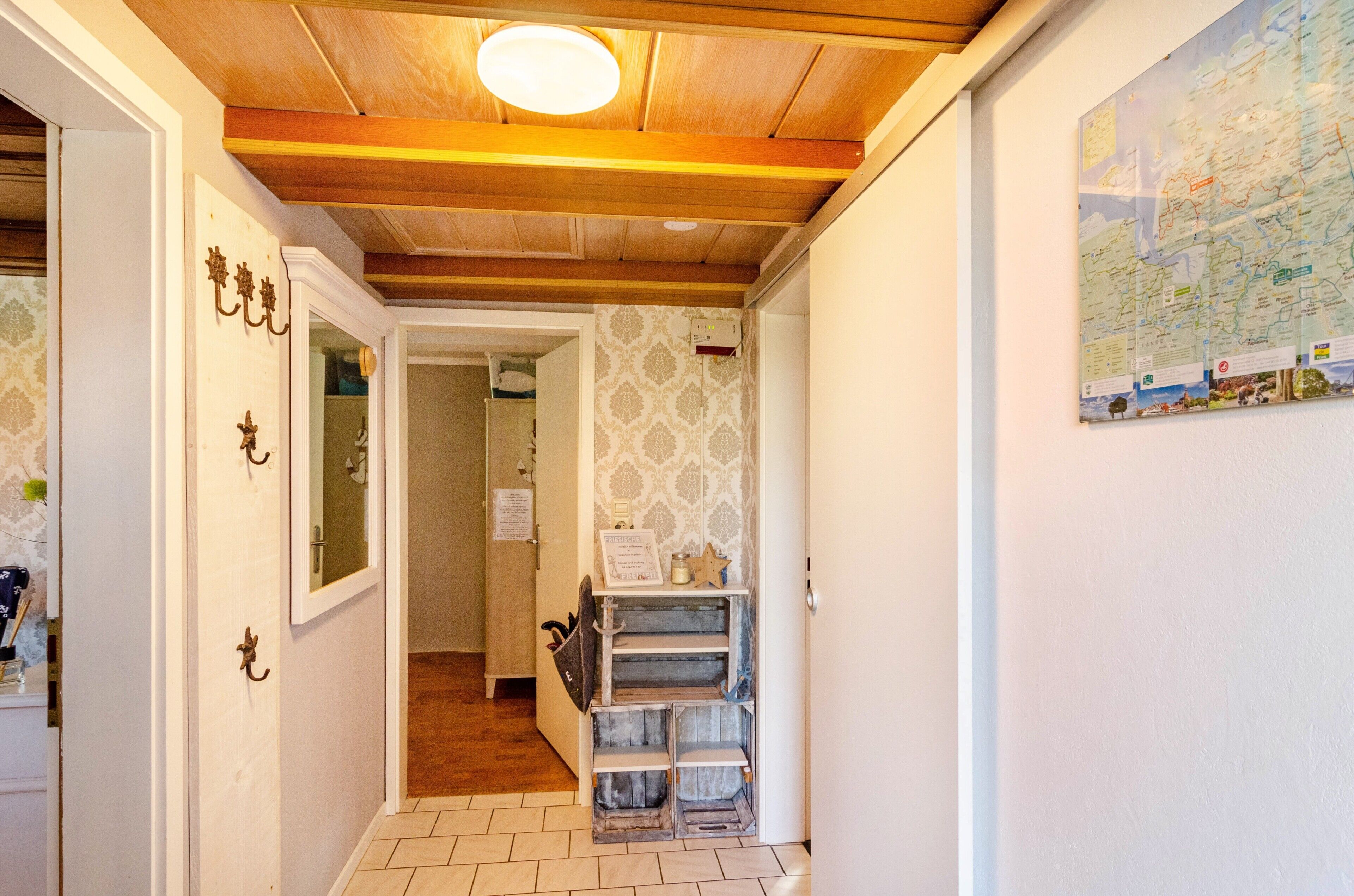 A narrow hallway with wooden ceiling beams, a map on the wall, and a small shelf with items.