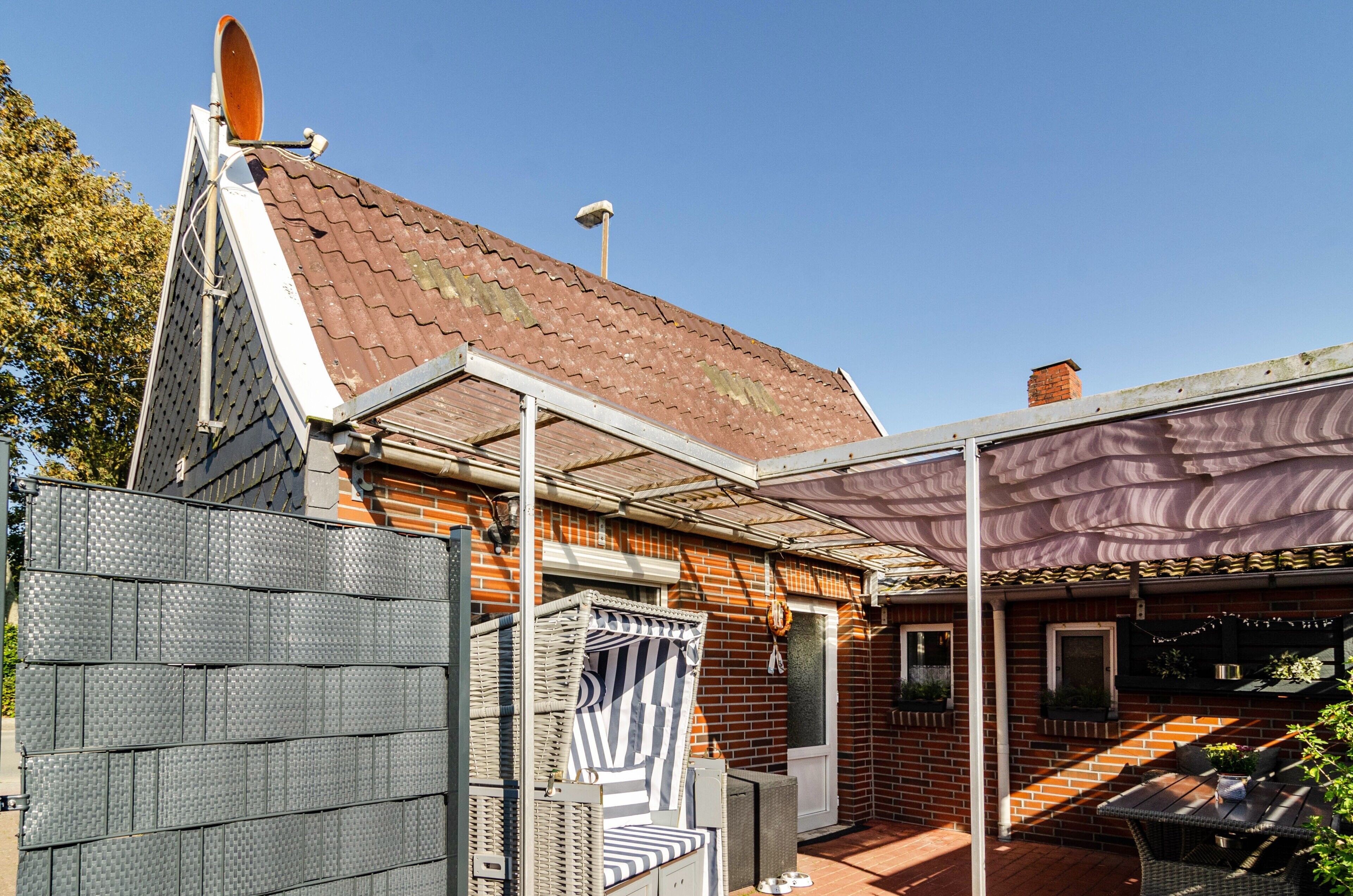 A house with a sloped roof, a covered patio area, and a fenced garden.