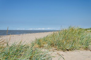 A beach with sand and grass in the foreground, a clear sky, and a calm sea in the background. - Vacation Home 'Segelboot' with Garden, BBQ & Wi-Fi (Krummhörn)