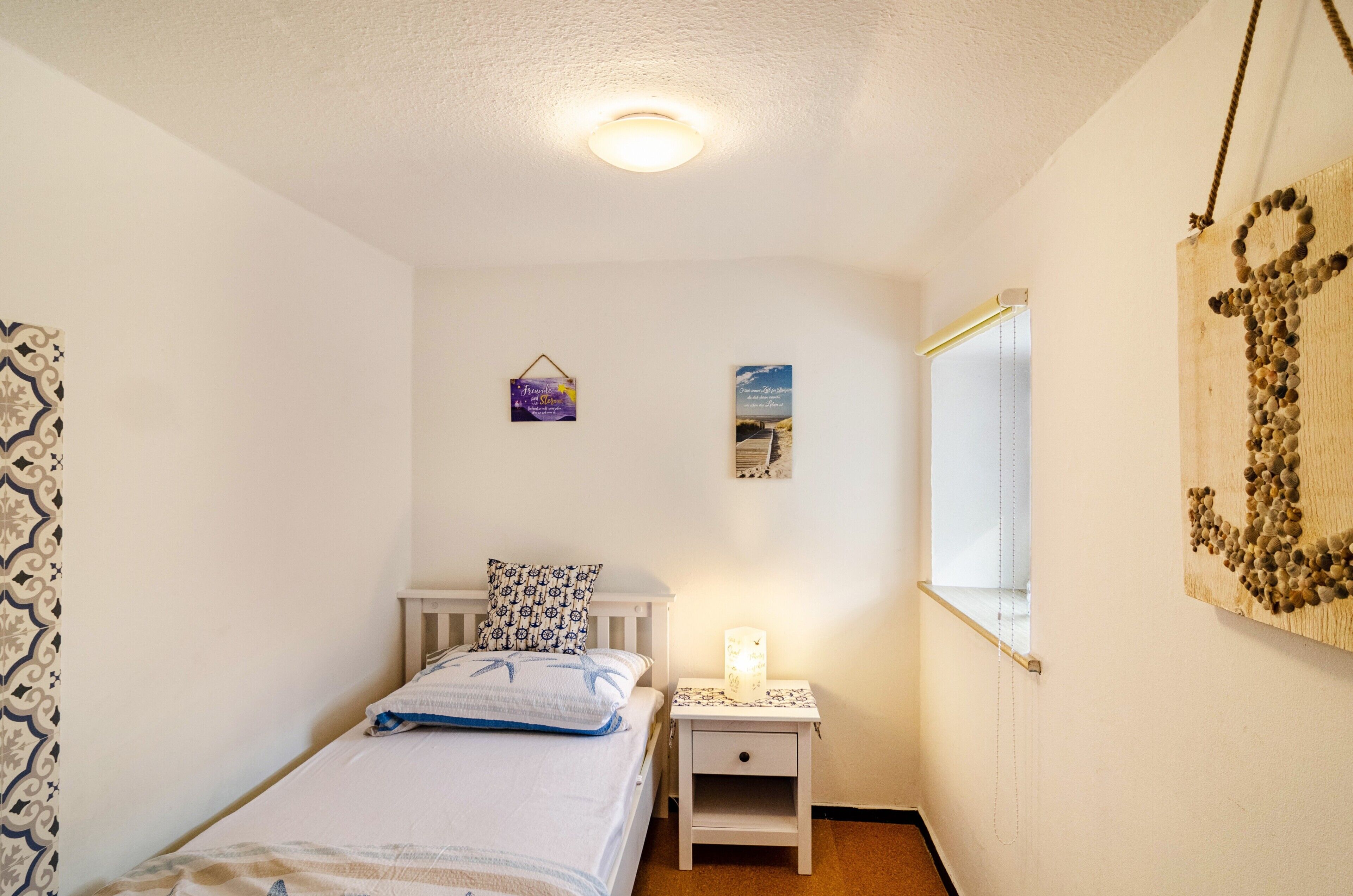 A bedroom with a bed, bedside table, wall art, and a window.
