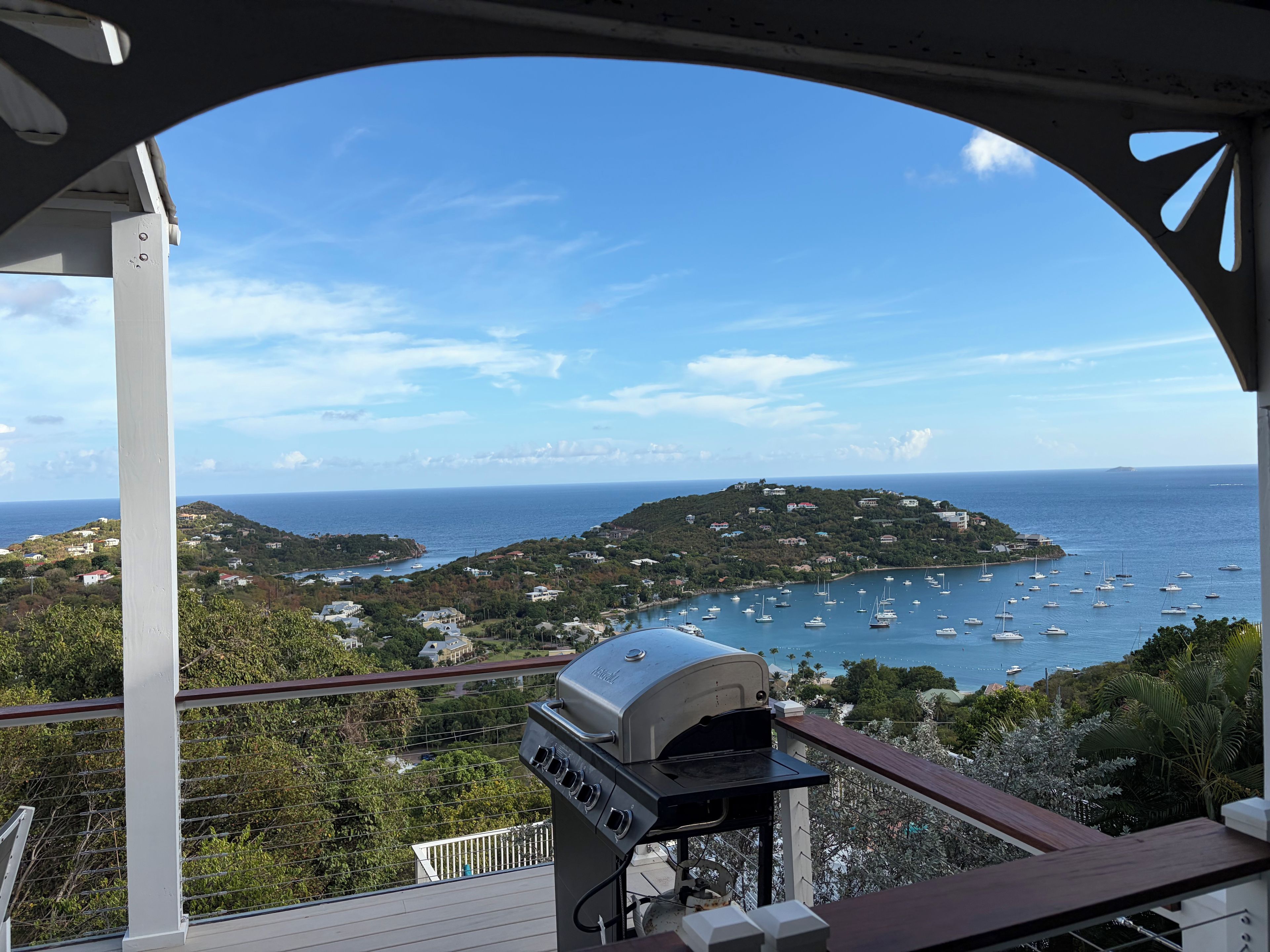 A balcony with a grill, overlooking a coastal landscape with boats and houses.