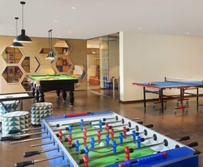 A room with a foosball table, a pool table, and a billiards table.