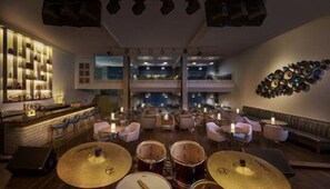 A multi-level bar area with a drum set, seating, and a wall of decorative plates.