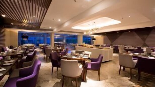A modern hotel dining area with multiple tables and chairs, a central buffet, and a view of the cityscape. - Le Méridien Goa, Calangute (Calangute)