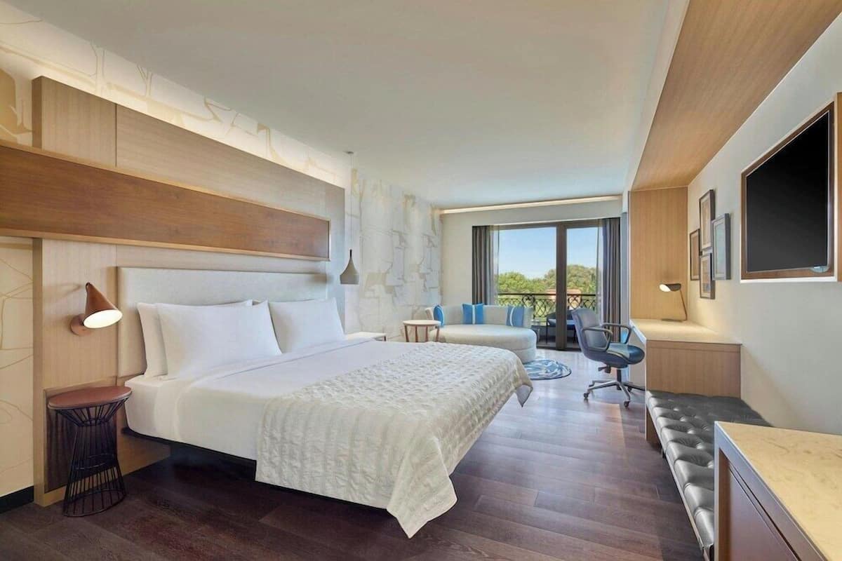 Une chambre d’hôtel moderne, dotée d’un grand lit, d’un bureau, d’une chaise et offrant une vue sur l’extérieur.