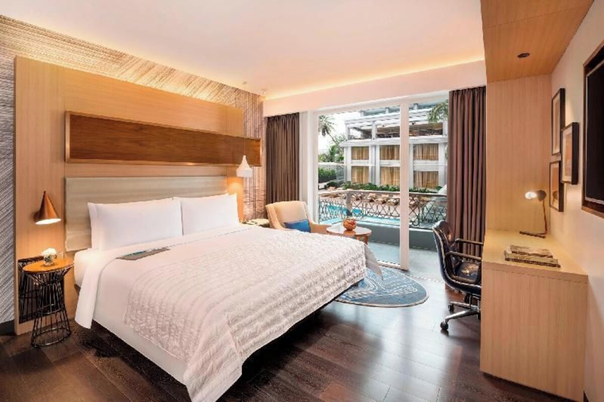Une chambre d’hôtel moderne dotée d’un grand lit, d’un bureau, d’une chaise et d’un balcon offrant une vue sur les bâtiments.