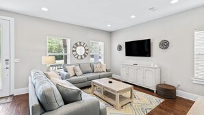 A modern living room with a grey sectional sofa, a wooden coffee table, and a TV on the wall. - 30A Getaway - Beach, Dining, Shopping Nearby - Sleeps 12 (Santa Rosa Beach)