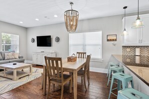 A modern kitchen with white cabinets, a wooden dining table, and blue bar stools. - 30A Getaway - Beach, Dining, Shopping Nearby - Sleeps 12 (Santa Rosa Beach)
