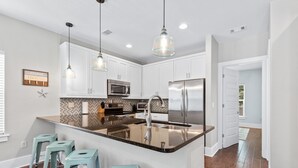A modern kitchen with white cabinets, a stainless steel refrigerator, a microwave, and a large island with bar stools. - 30A Getaway - Beach, Dining, Shopping Nearby - Sleeps 12 (Santa Rosa Beach)
